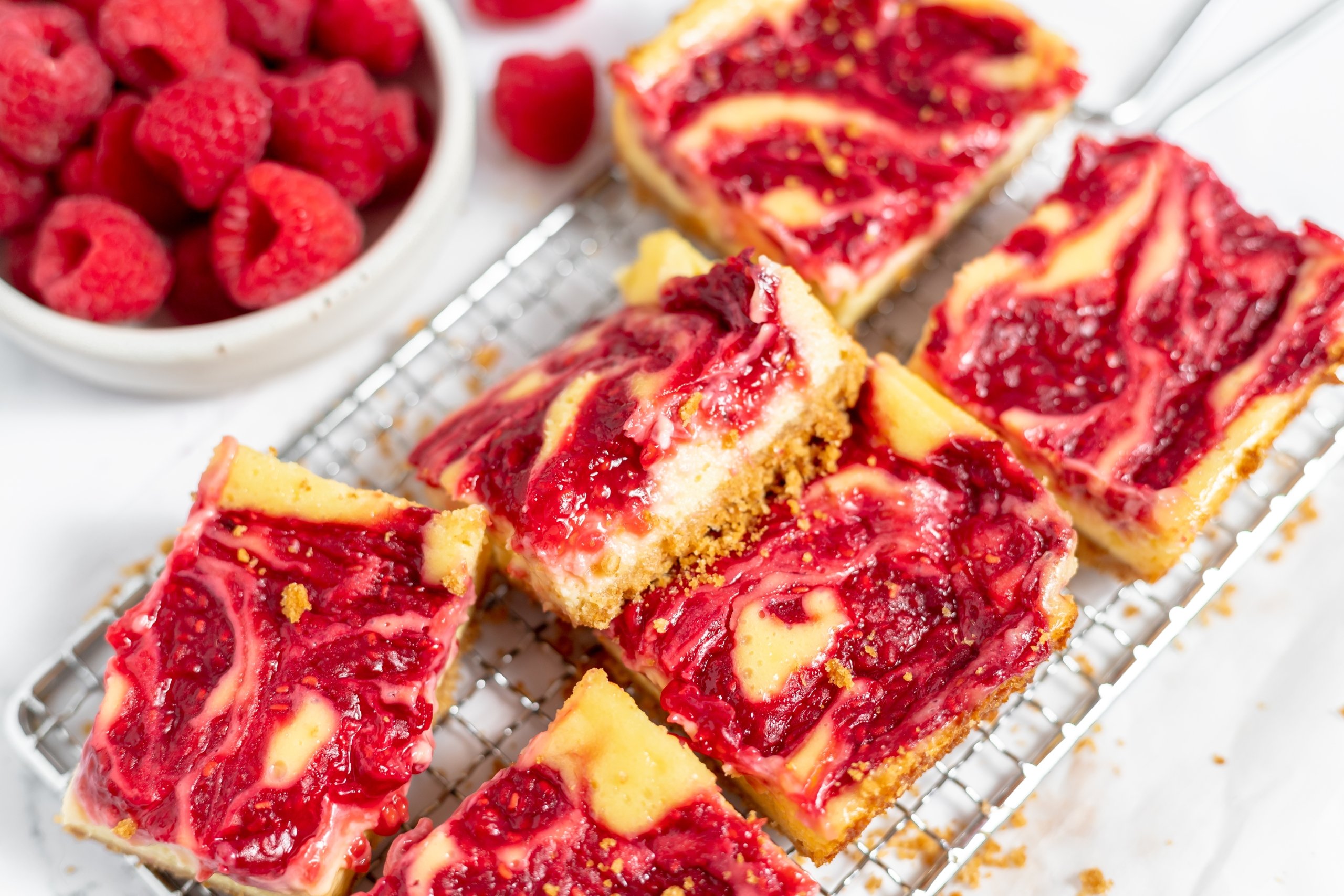 angle view of raspberry cheesecake bars on a wire rack