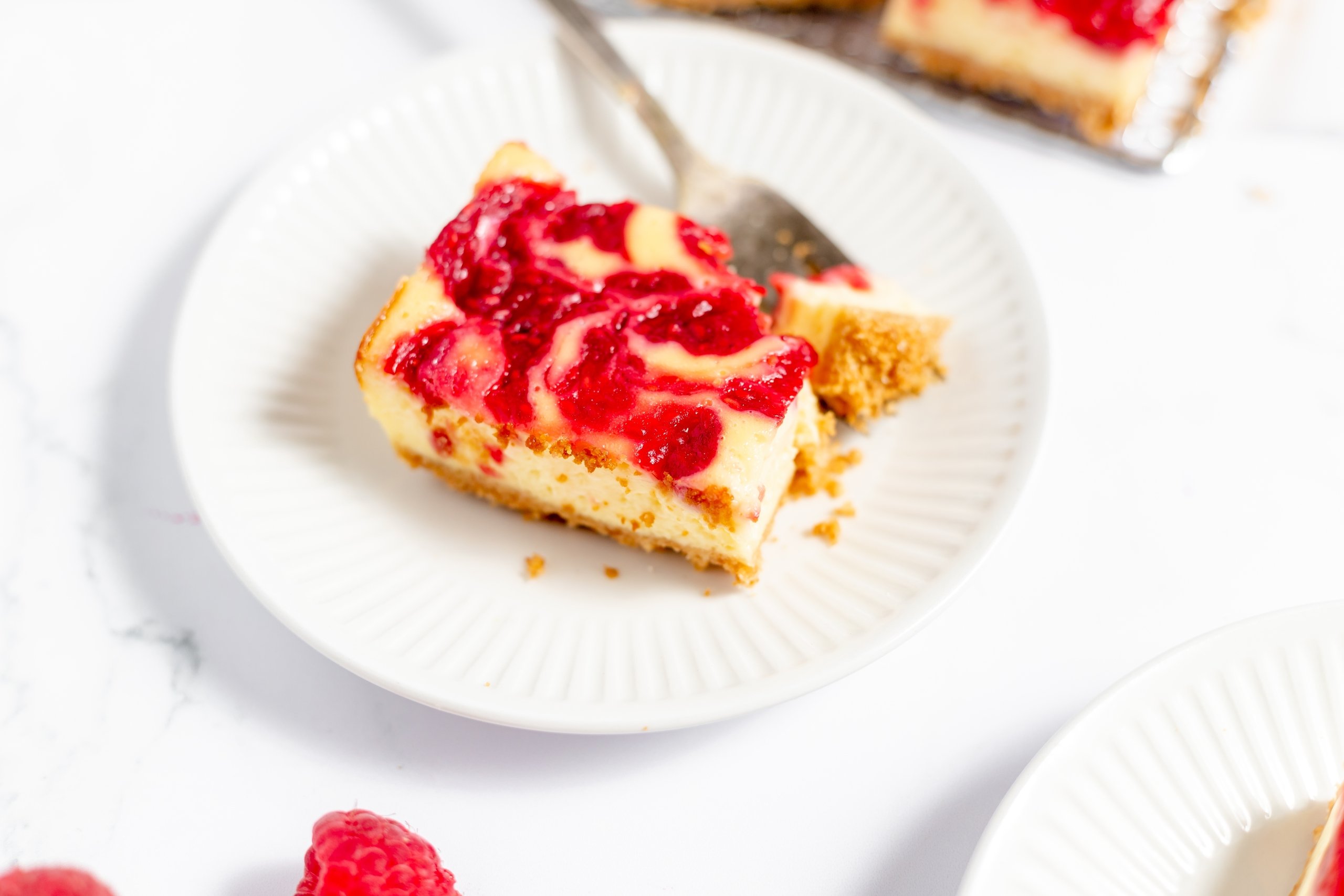 close up of raspberry cheesecake bar on a small white plate