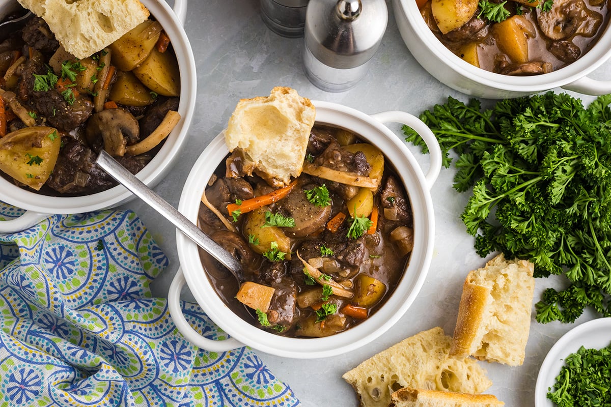 overhead shot of spoon in crock of red wine beef stew with crusty bread
