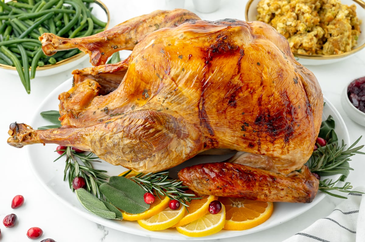 browned turkey on a serving platter with oranges, cranberry and herbs