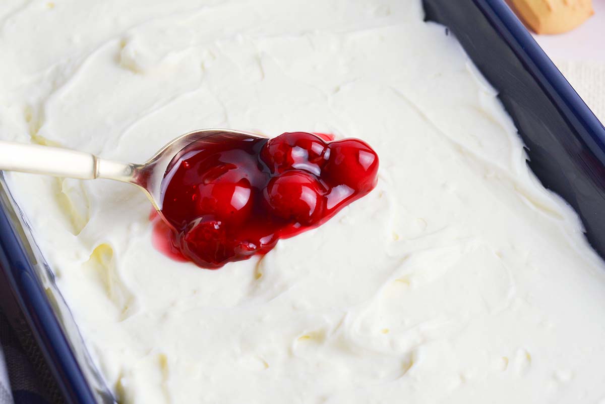 spooning cherry pie filling onto cheesecake dip