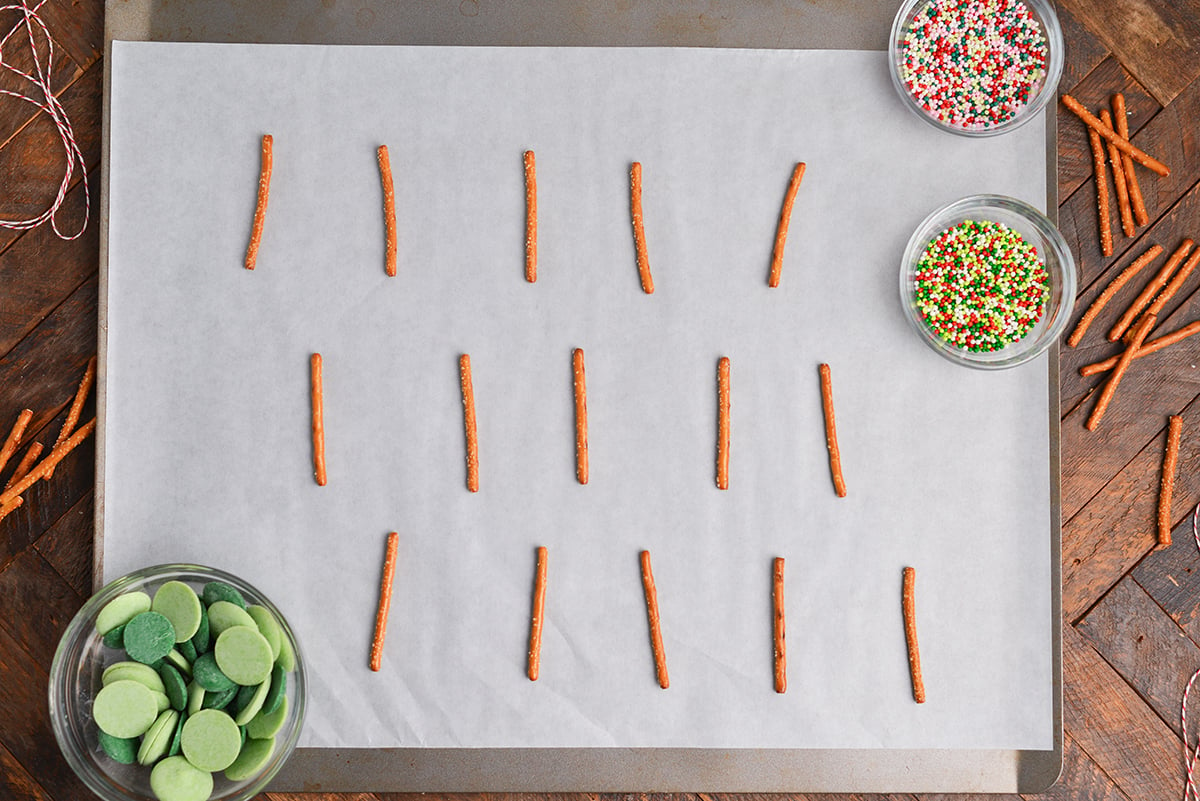pretzels sticks laid out on parchment with sprinkles and green melting chocolate