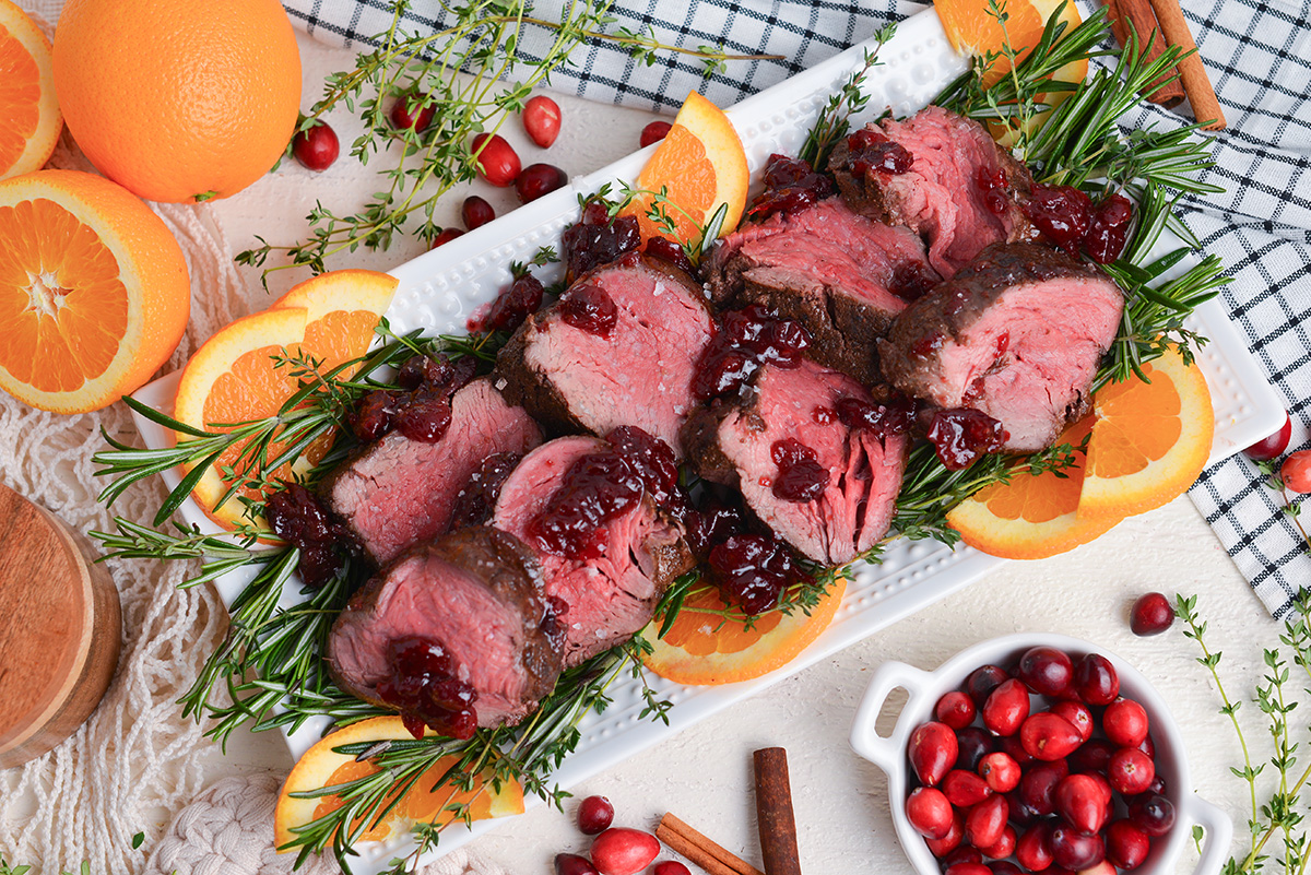 sliced beef fillets on a serving platters with orange slices and fresh rosemary