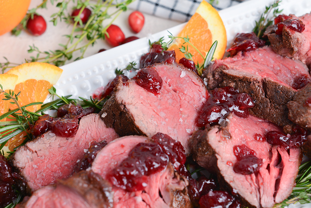 angle close up of rare beef tenderloin with cranberry sauce and fresh herbs