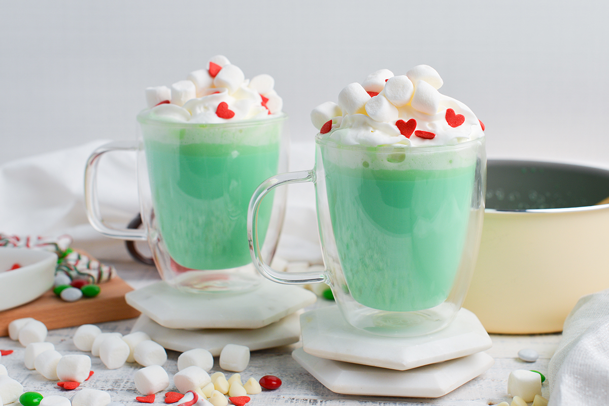two green hot chocolates with whipped cream, marshmallows and red hearts sprinkles