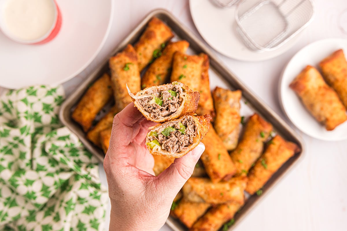 overhead shot of hand holding two philly cheesesteak egg roll halves