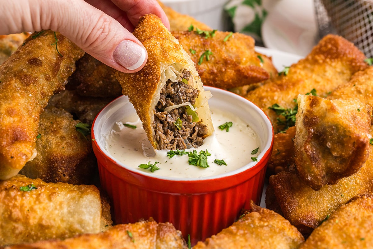 hand dipping egg roll into white sauce