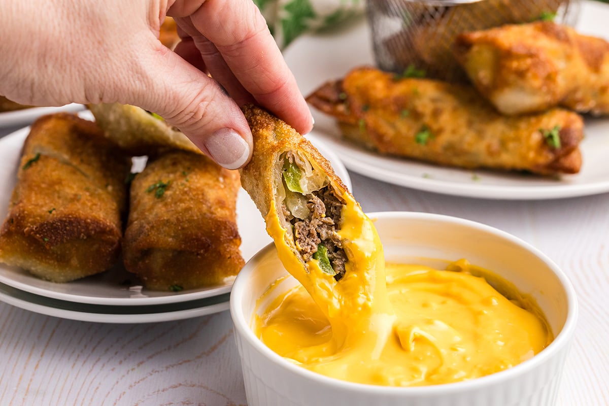 hand dipping egg roll into bowl of sauce