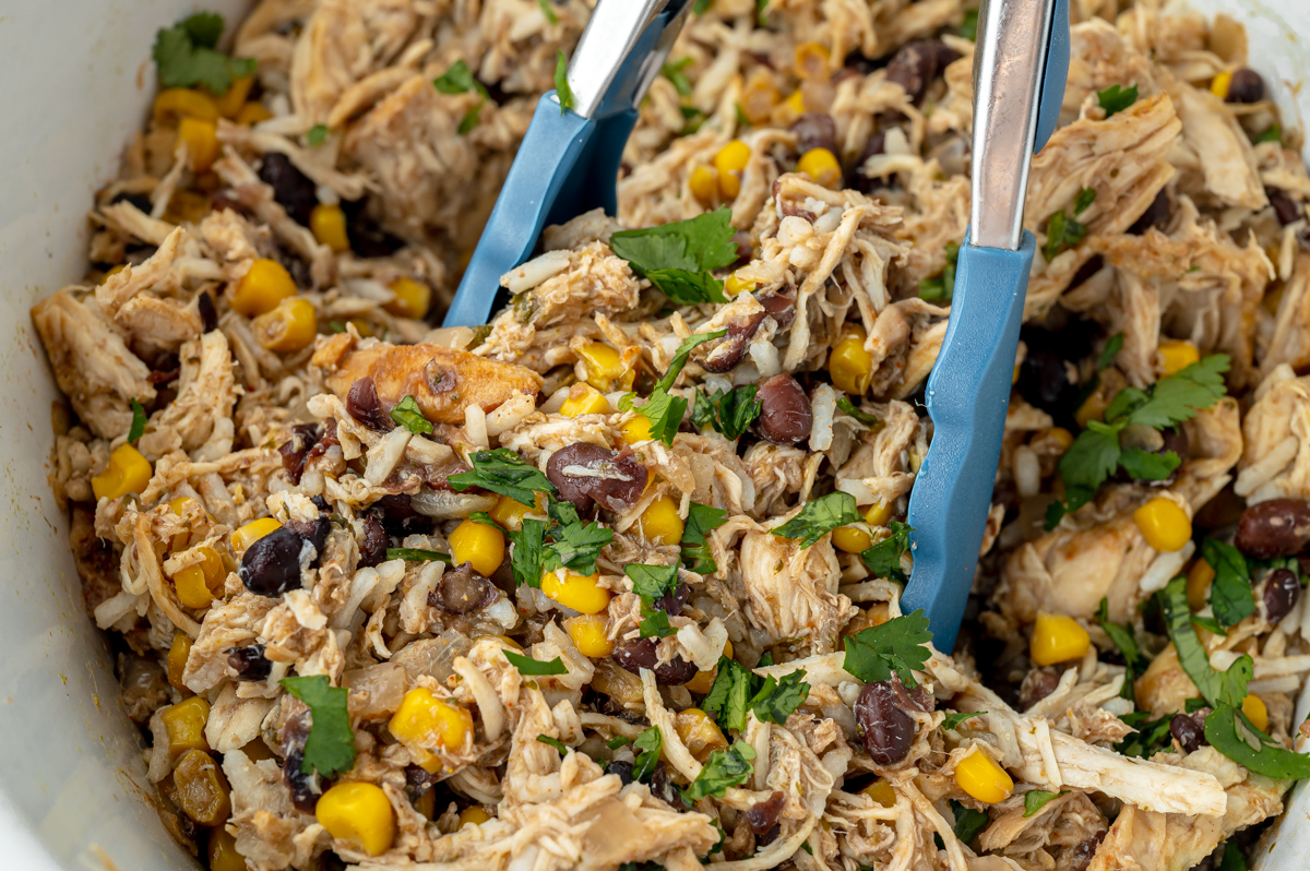 tongs tossing shredded taco chicken in crock pot