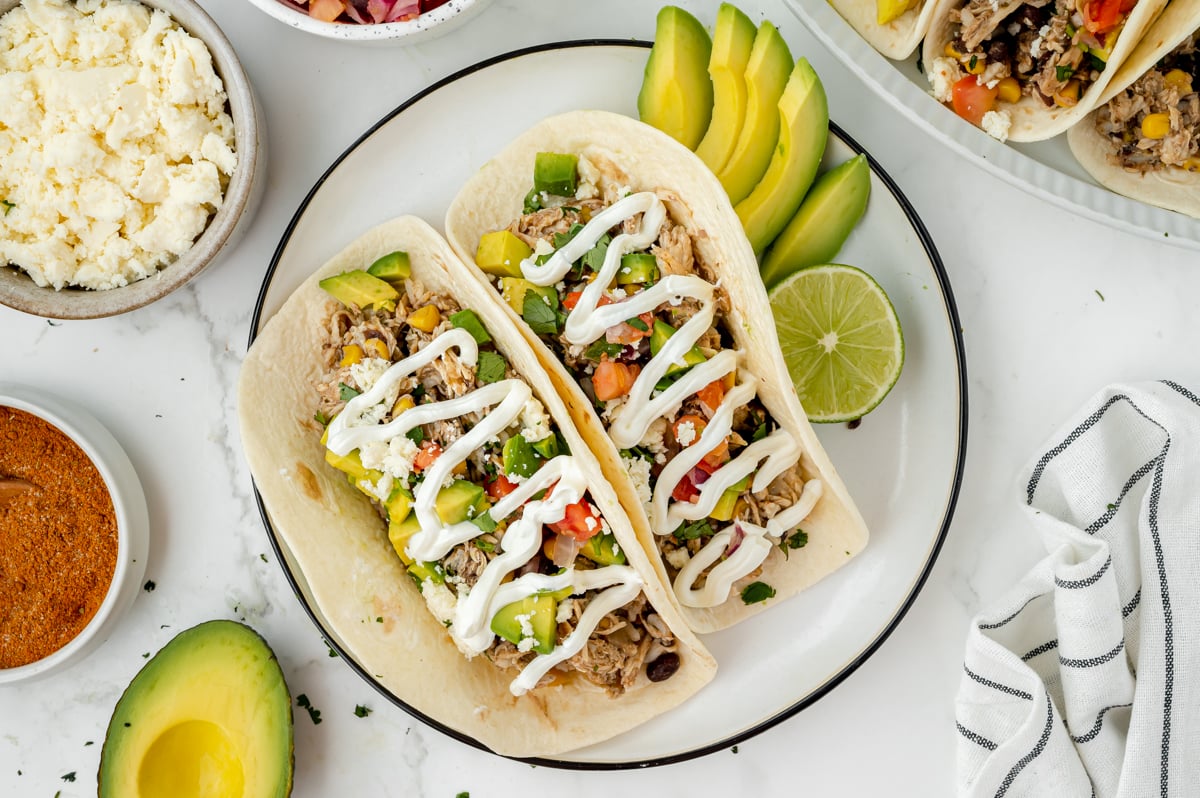 overhead shot of two chicken tacos on plate with avocado and lime