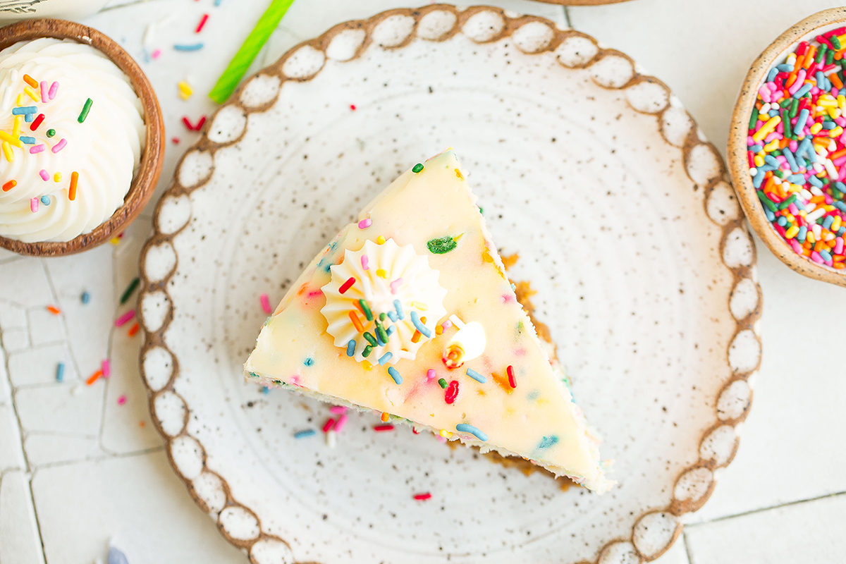 overhead slice of rainbow cheesecake on a white ceramic plate