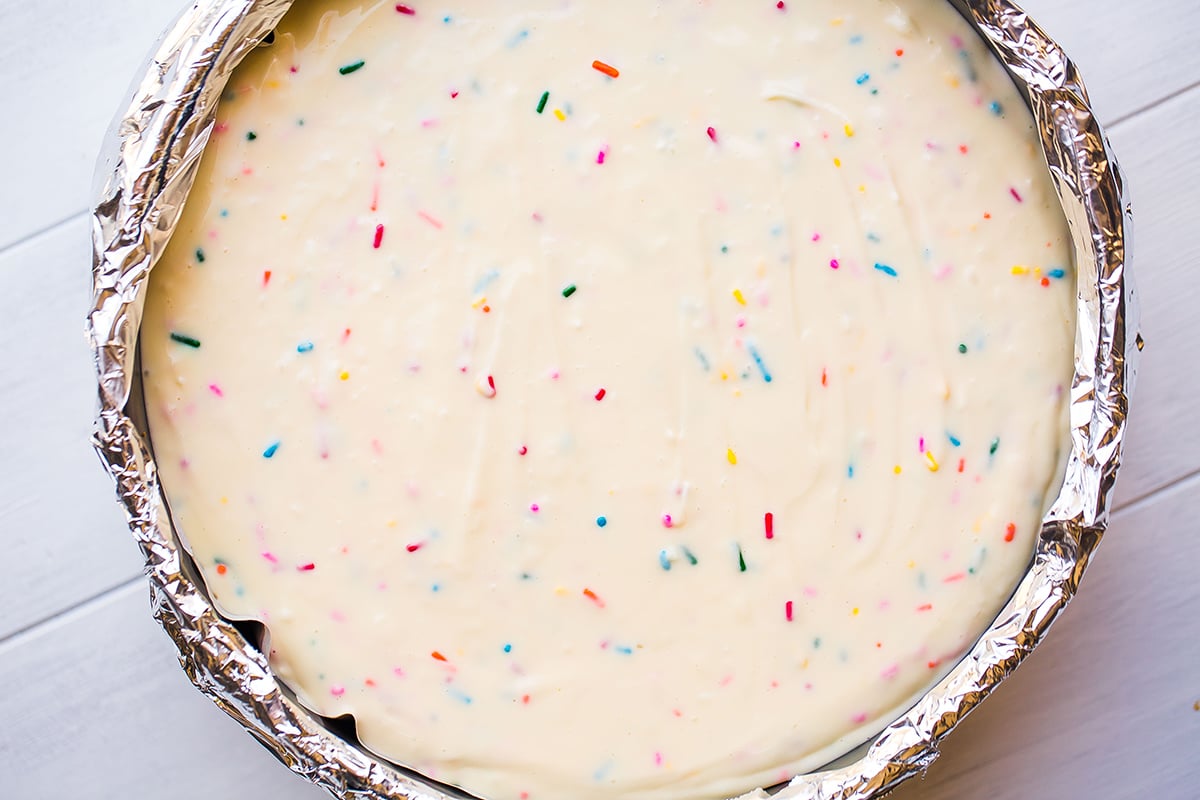 cheesecake batter with rainbow sprinkles spread into aluminum foil lined springform pan