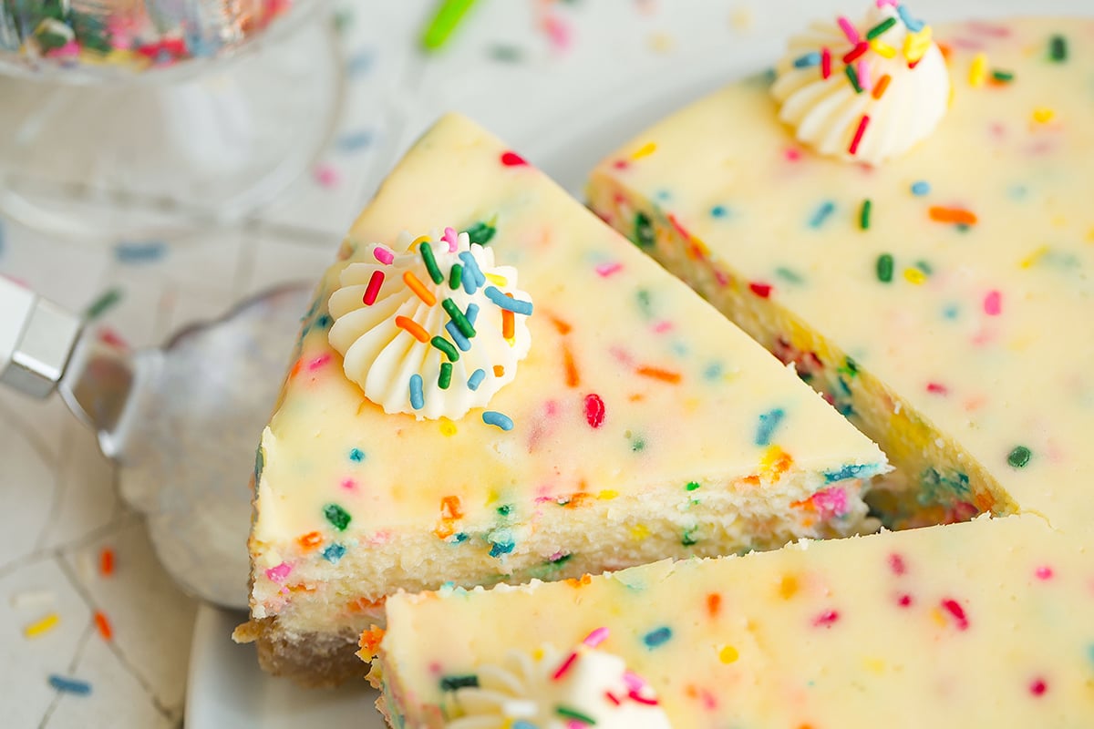 spatula lifting a slice of cheesecake with rainbow sprinkles