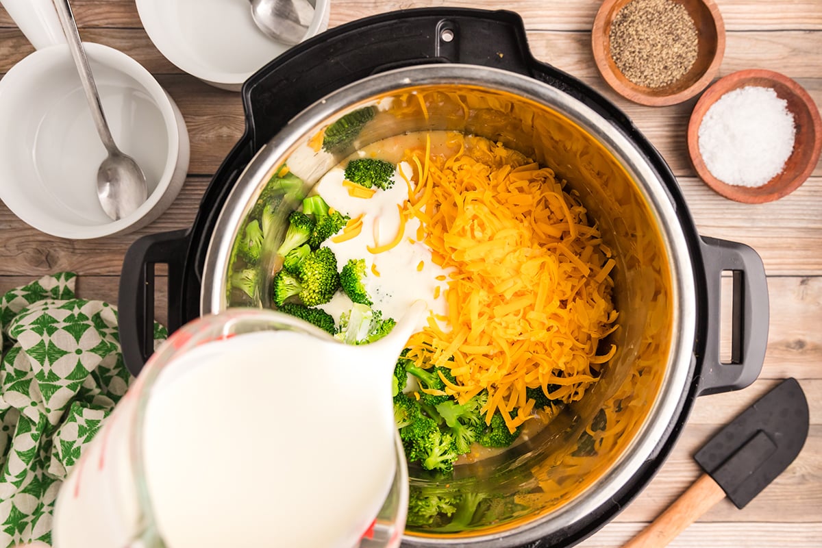 pouring cream into the bowl of an instant pot over cheese, broccoli and soup