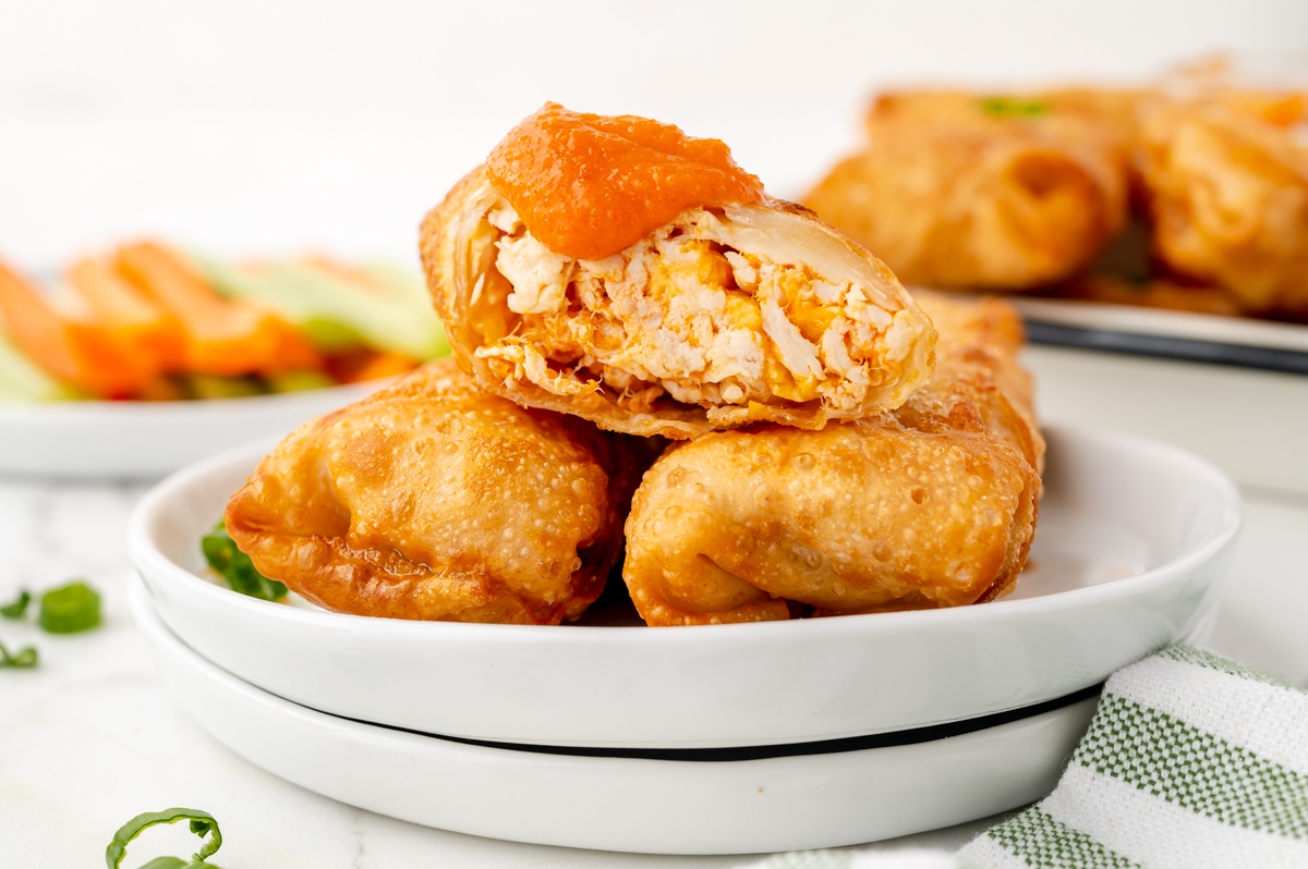 three buffalo chicken egg rolls on plate topped with buffalo sauce