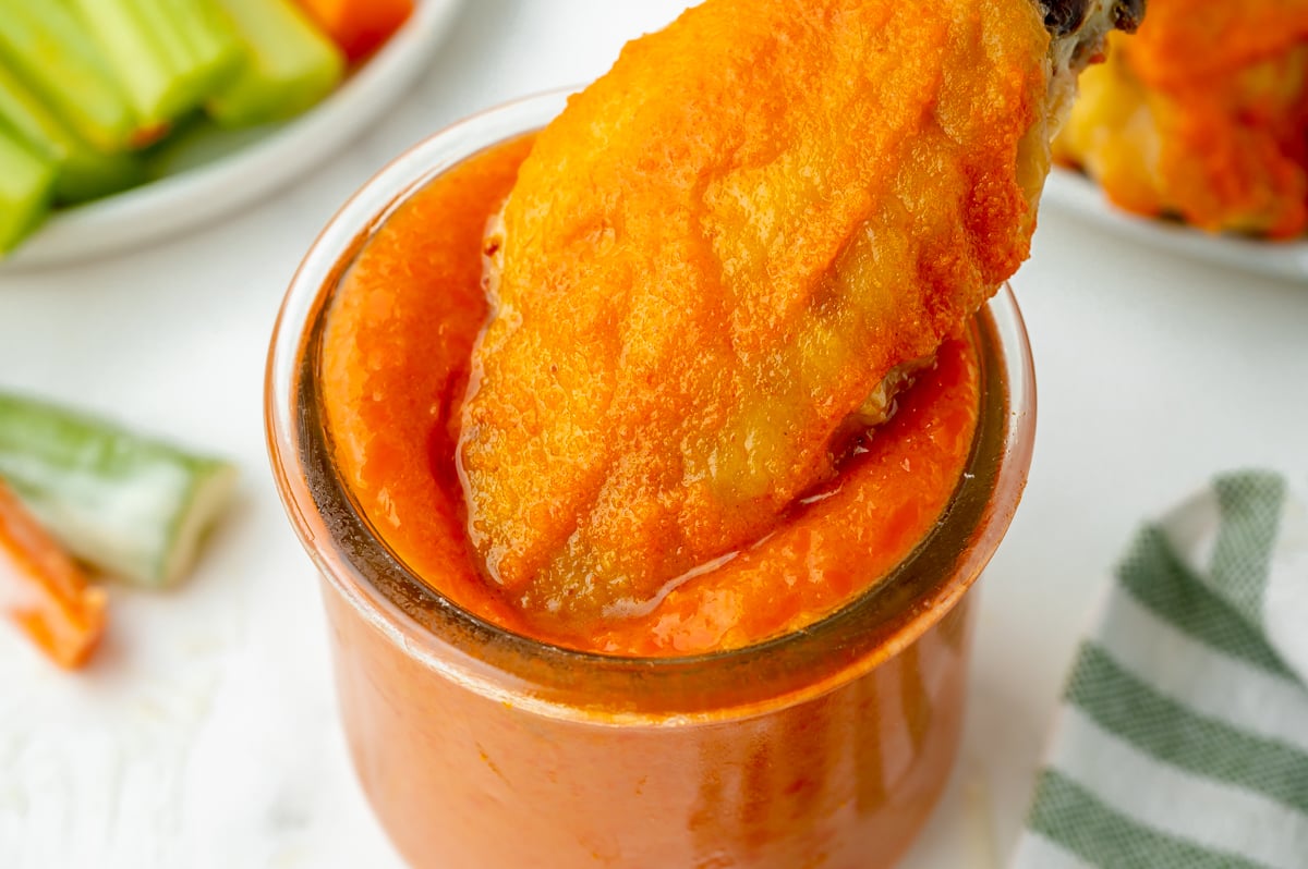 close up of wing dipping into buffalo sauce