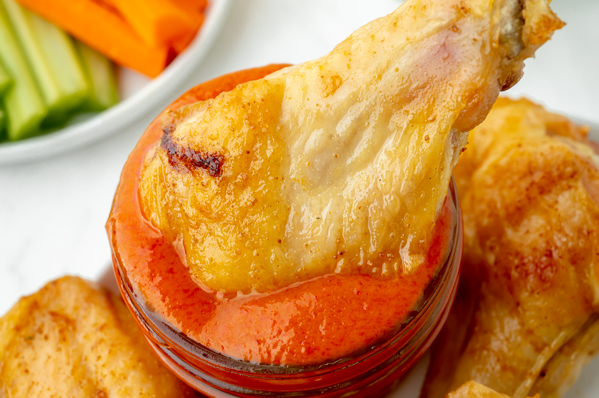 baked buffalo wing dipping into jar of buffalo sauce