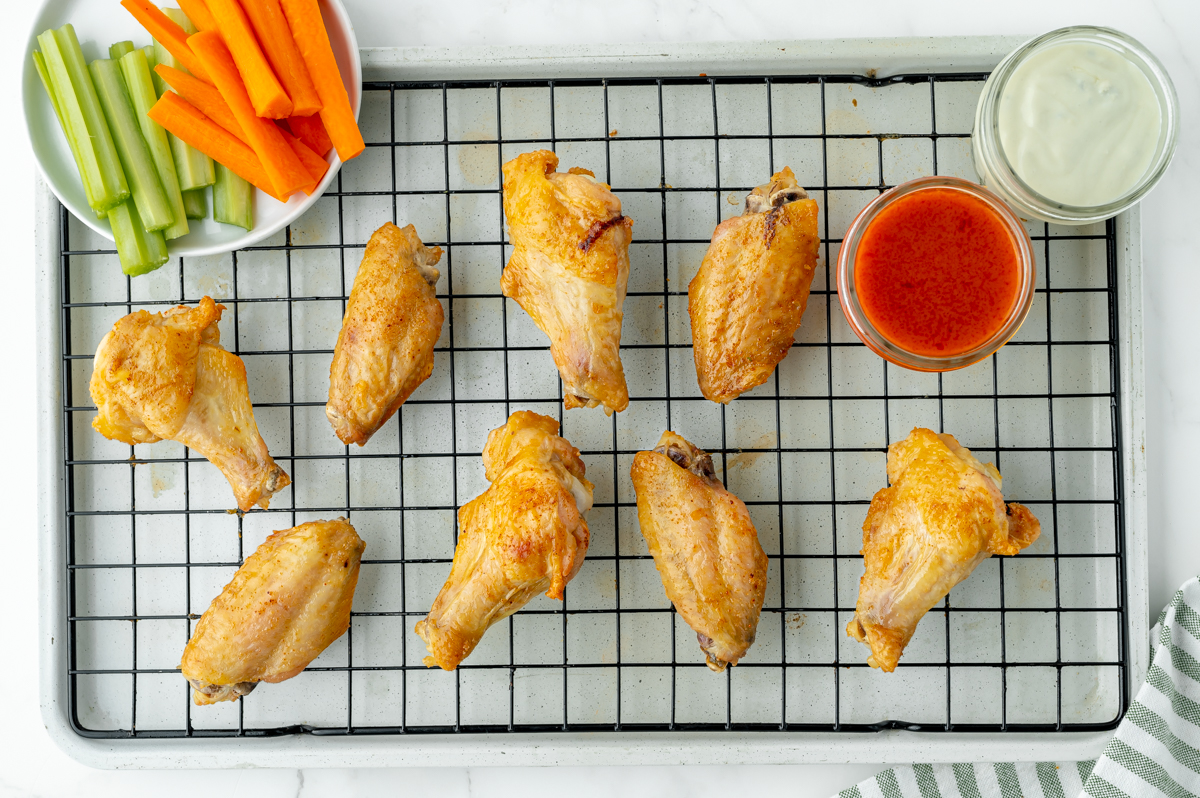 overhead shot of baked buffalo wings on wire rack with sauce and celery and carrots