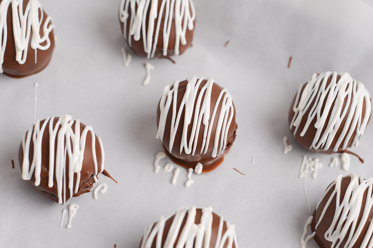 close up angled shot of white chocolate drizzled onto chocolate cheesecake bites