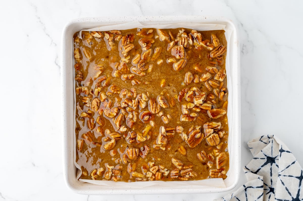 pecan pie filling poured over pecans in pan