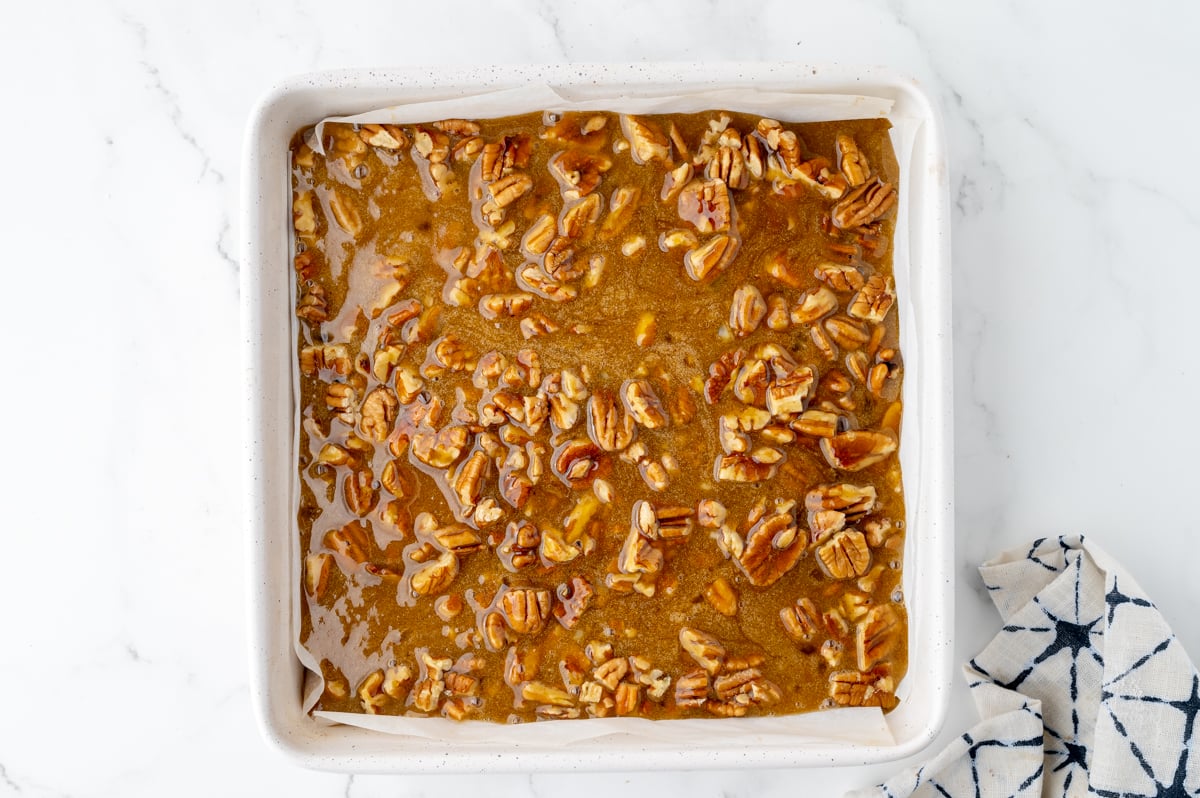 pecan pie filling poured over pecans in pan