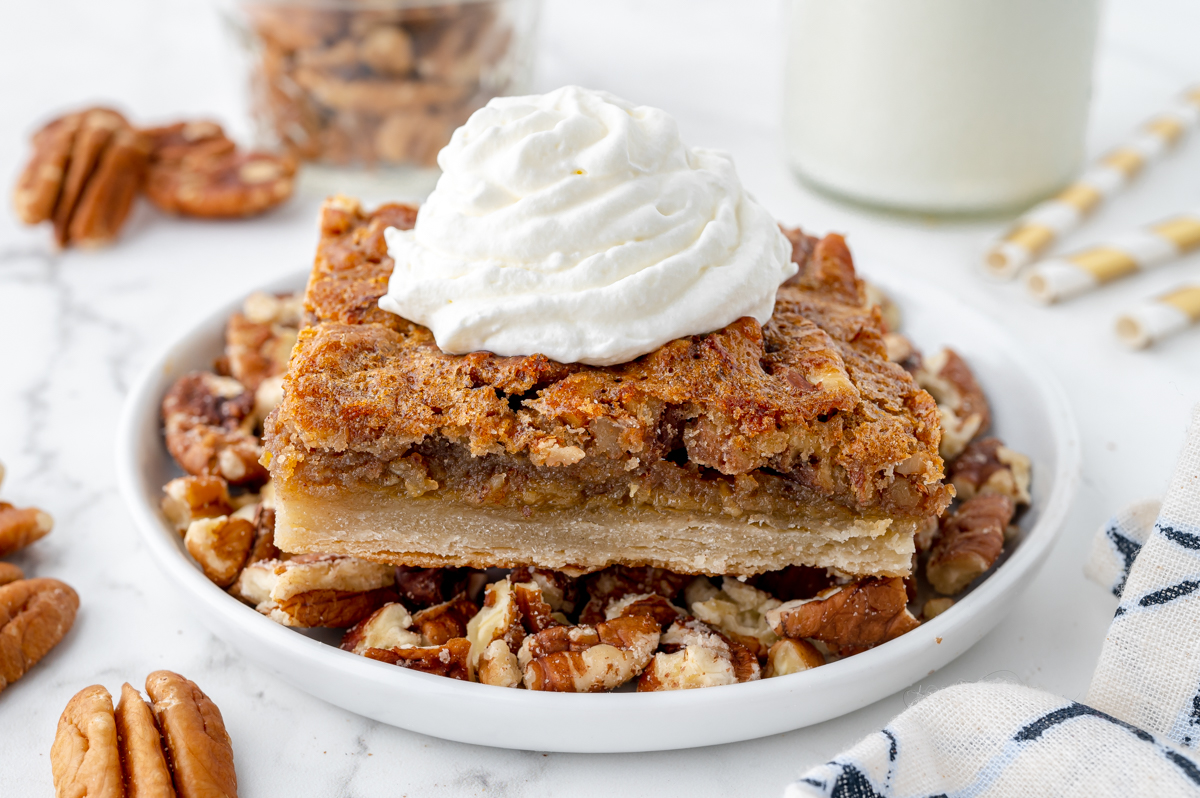 angled shot of pecan pie bar on plate topped with whipped cream