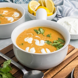 angled shot of bowl of red lentil soup on wooden board