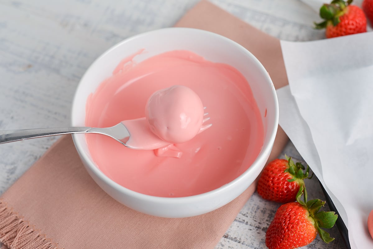 cheesecake bite dipped into bowl of melted pink chocolate