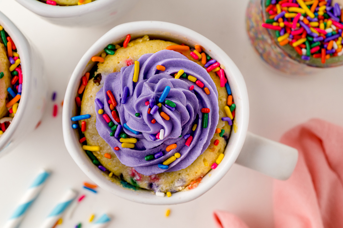 overhead of a mug cake with purple frosting and sprinkles