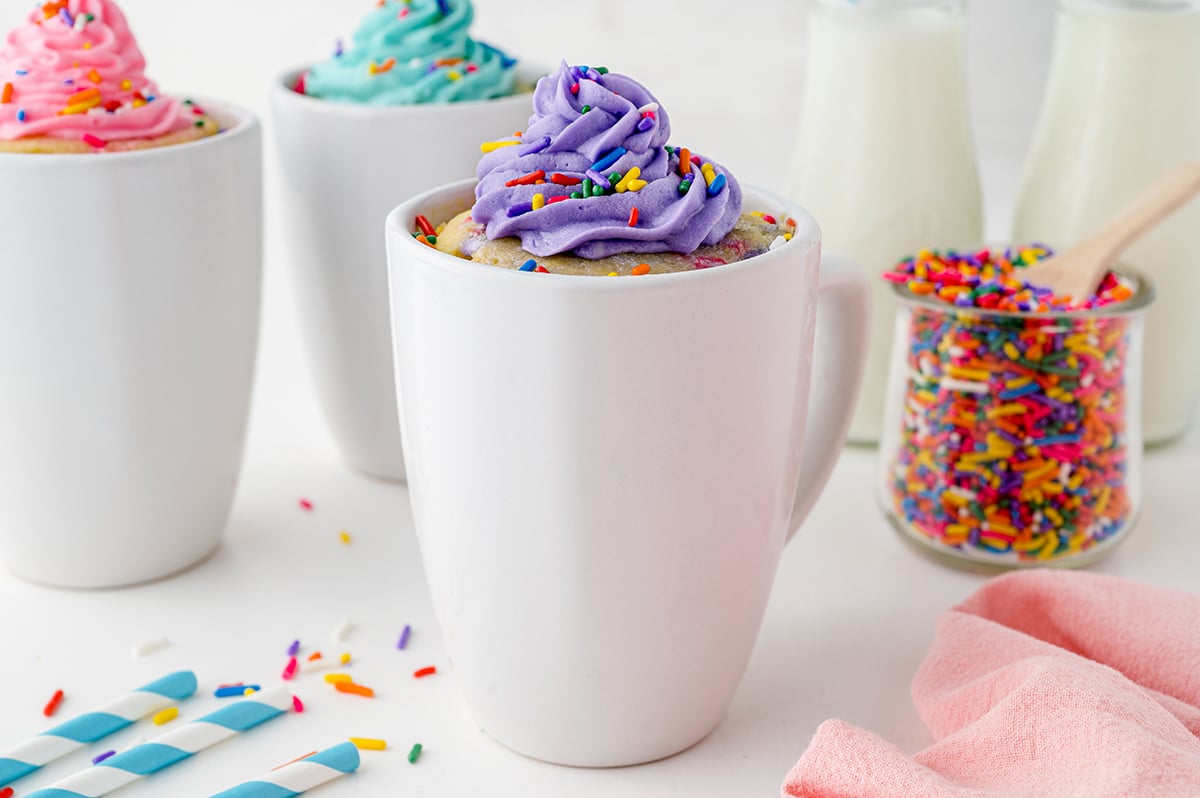 head on shot of three mug cakes with bright frosting and sprinkles