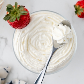 overhead shot of bowl of homemade whipped cream with strawberry and spoon