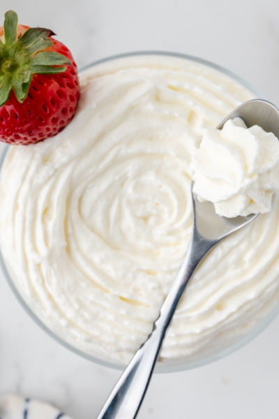 overhead shot of bowl of homemade whipped cream with strawberry and spoon