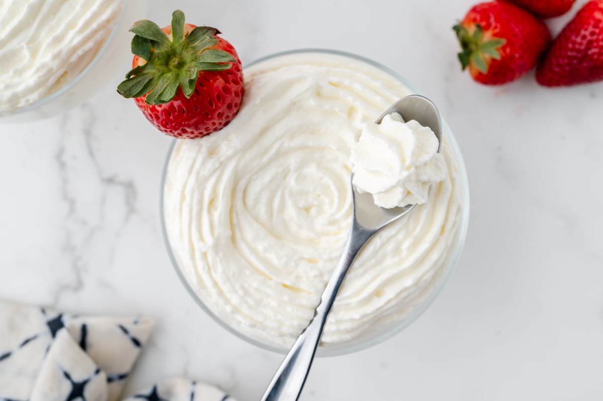 overhead shot of bowl of homemade whipped cream with strawberry and spoon