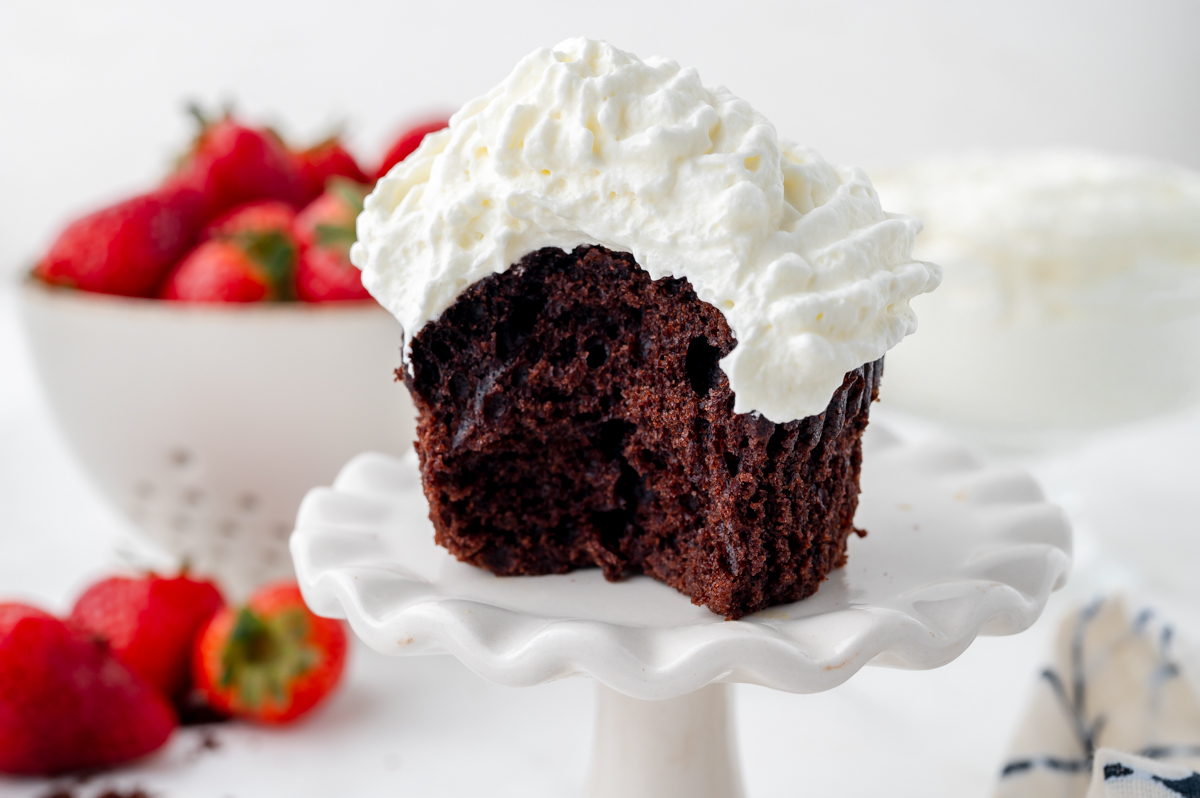 bite taken out of chocolate cupcake topped with whipped cream