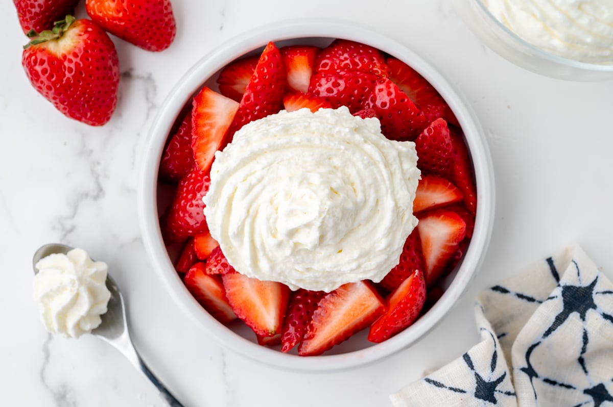 overhead shot of bowl of strawberries topped with homemade whipped cream