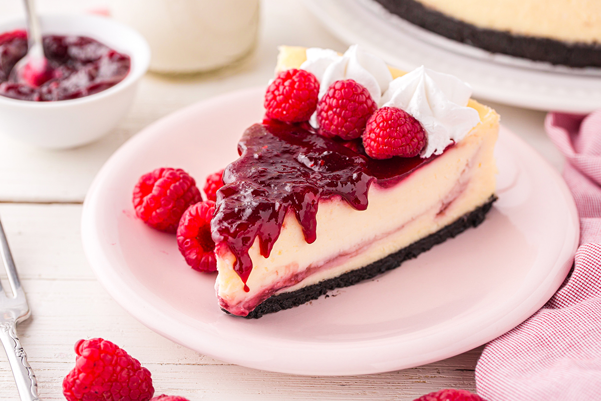angled shot of slice of cheesecake topped with raspberry sauce