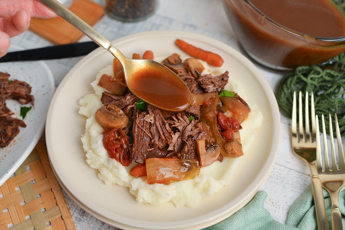 angled shot of spoon adding sauce to balsamic pot roast on a plate