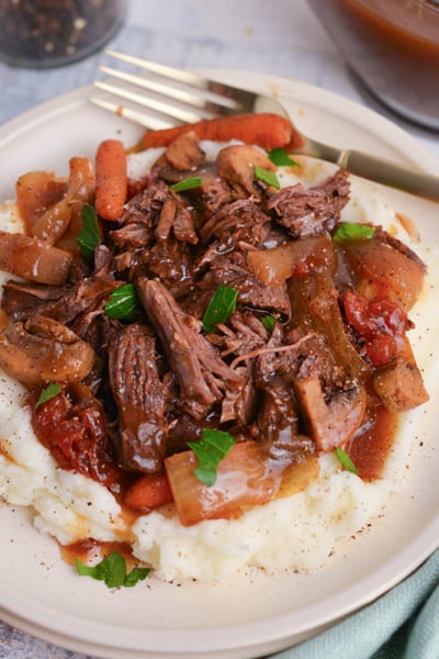 close up angled shot of balsamic pot roast over mased potatoes on plate