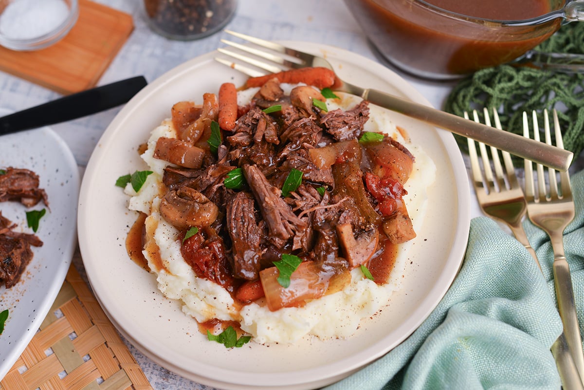 close up angled shot of balsamic pot roast over mased potatoes on plate