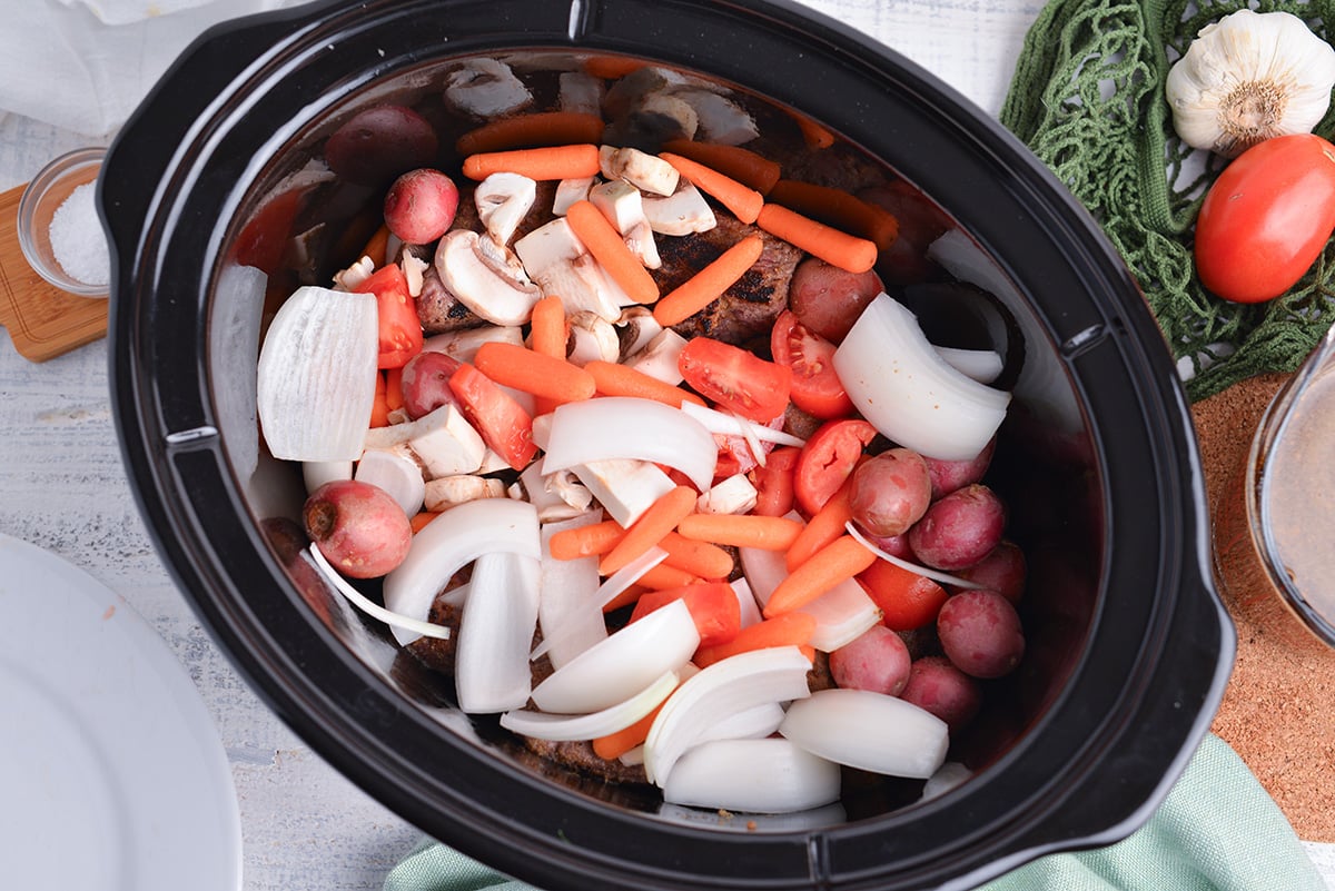 overhead shot of raw veggies added to slow cooker