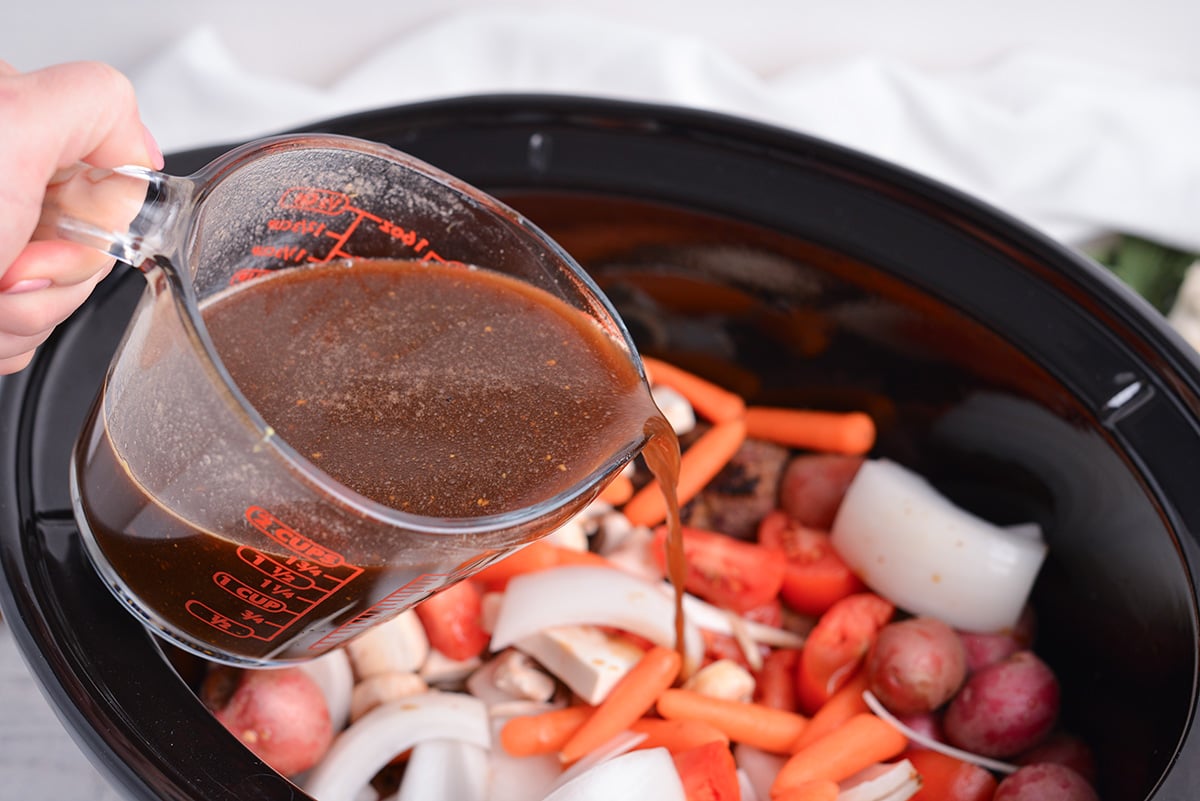 angled shot of broth poured into slow cooker of vegetables