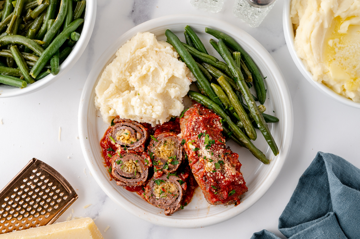 overhead shot of sliced beef braciole on plate with potatoes and green beans