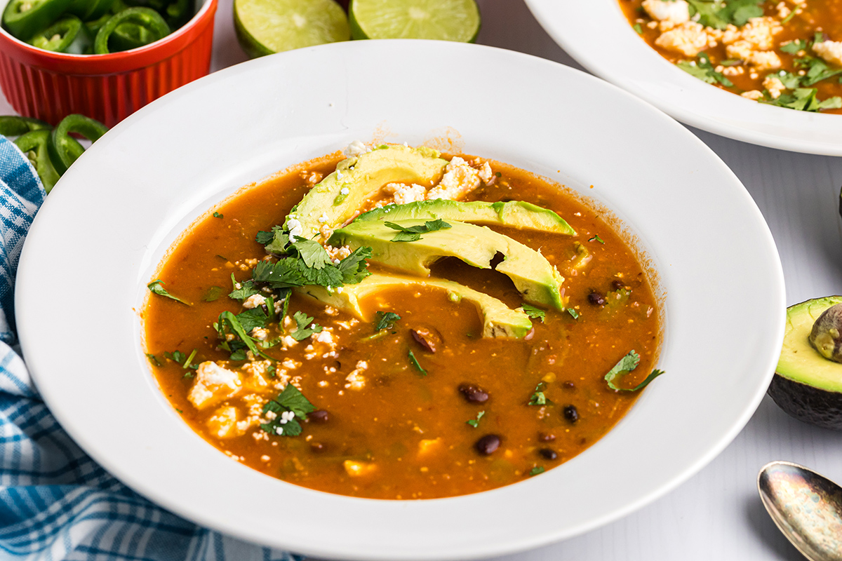 angled shot of black bean soup topped with avocado