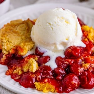 close up of cherry dump cake with vanilla ice cream scoop on top