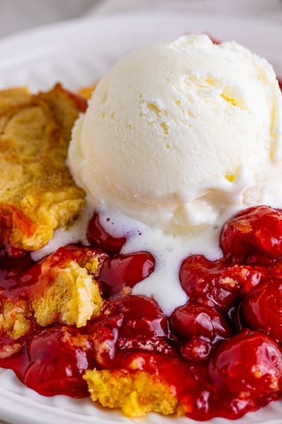 close up of cherry dump cake with vanilla ice cream scoop on top