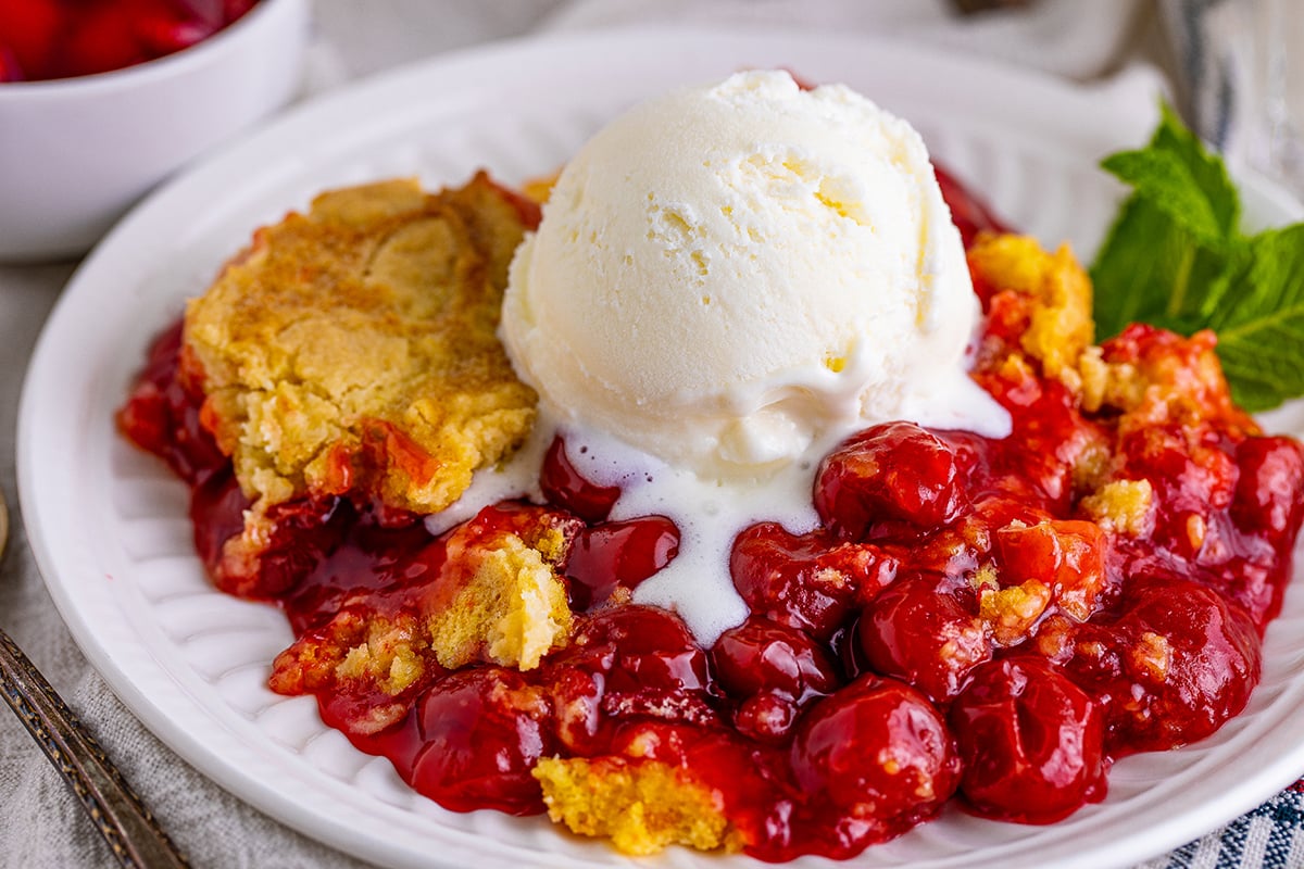 close up of cherry dump cake with vanilla ice cream scoop on top