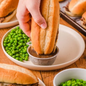 straight on shot of hand dipping french dip sandwich into cup of au jus