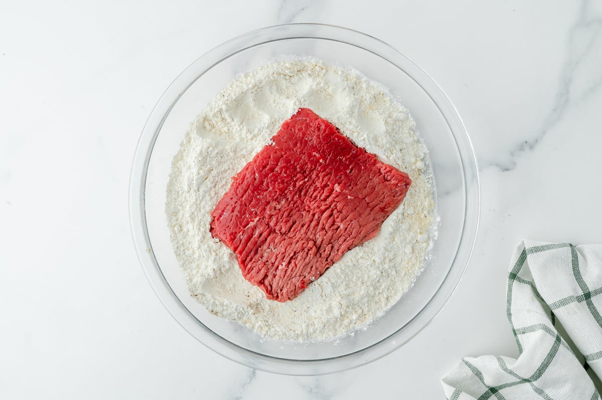 overhead shot of beef in bowl of flour