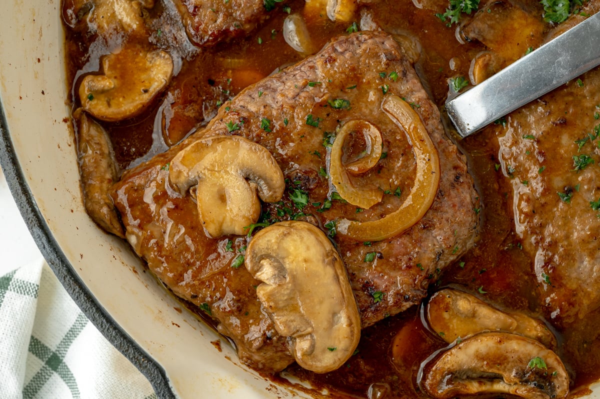 close up overhead shot of serving spoon in pan of cube steak