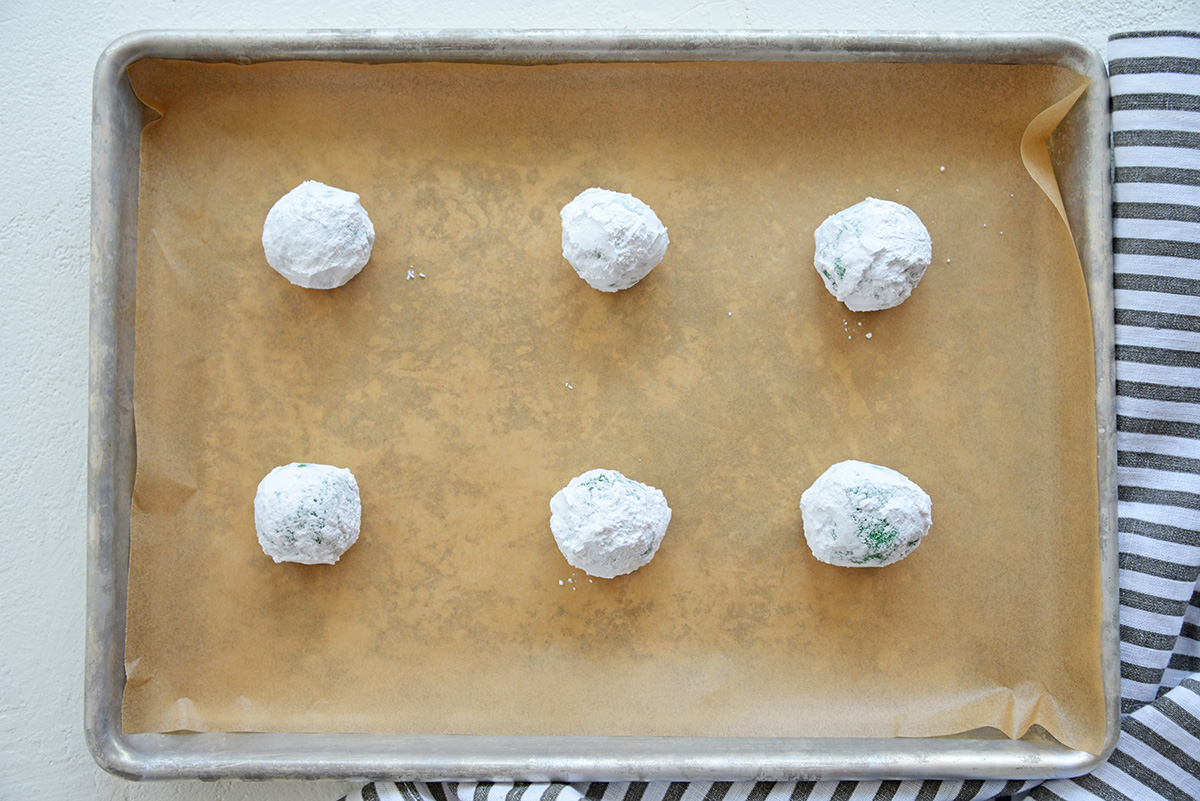 cookie dough balls coated in powdered sugar on parchment paper